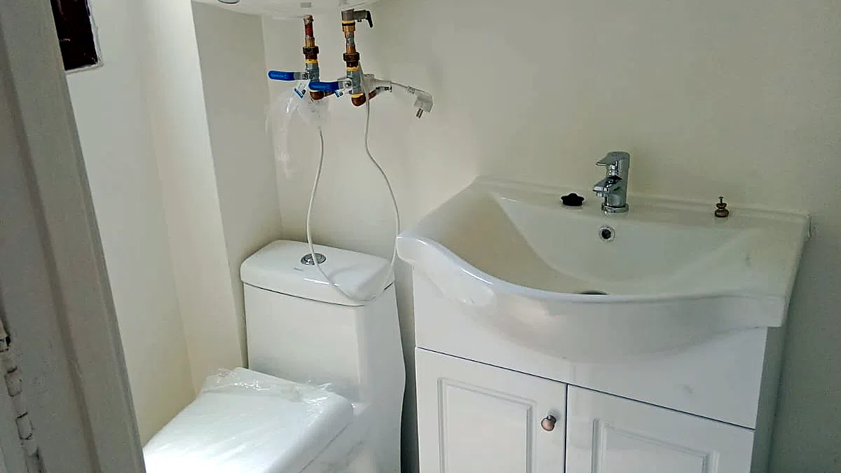 DESPUÉS: el baño remodelado con muros nuevos pintados, lavamanos con mueble y grifería monomando nuevos, WC nuevo y las instalaciones de agua renovadas a la vista.