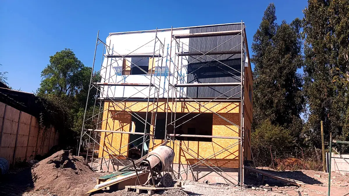 Casa de dos pisos en obra de Construcasa, con andamios y la techumbre y el revestimiento en ejecución, cubierta de plancha metálica y paneles OSB.