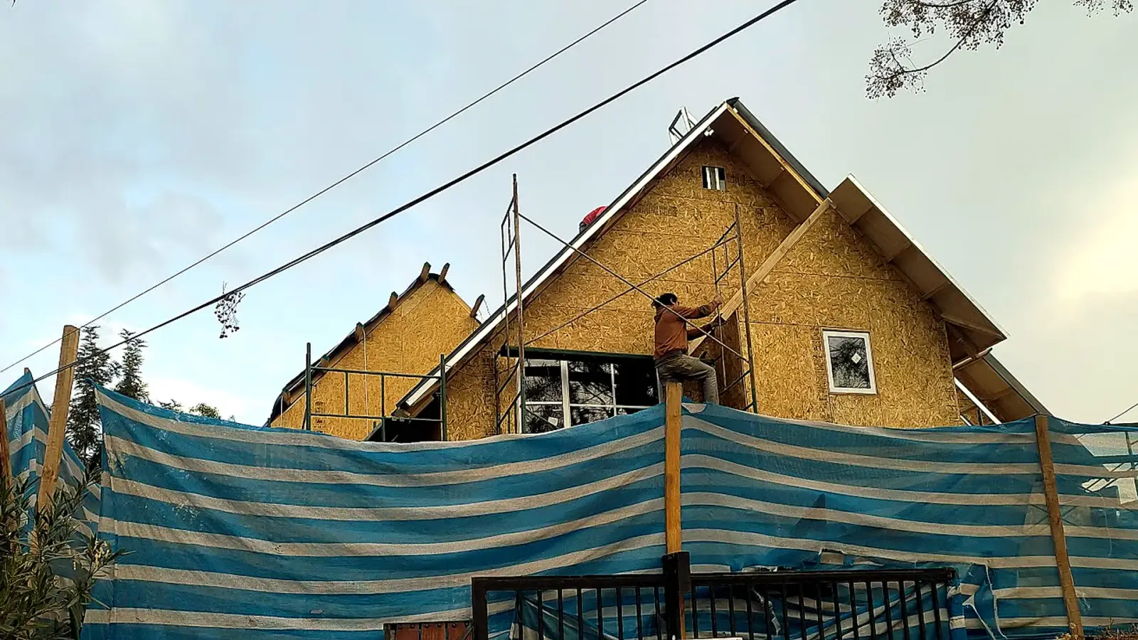 Trabajador de Construcasa en andamios sobre la fachada de OSB de una casa en construcción, con techumbre a dos aguas.