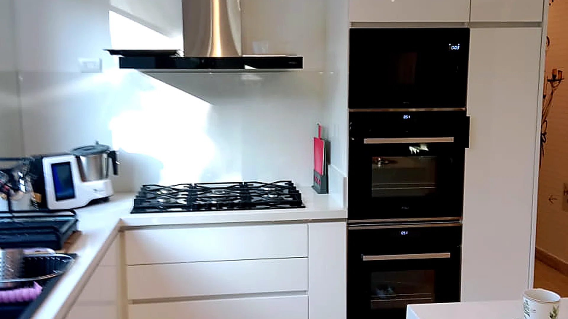 Cocina remodelada con muebles blancos, encimera a gas, campana de acero y hornos empotrados.