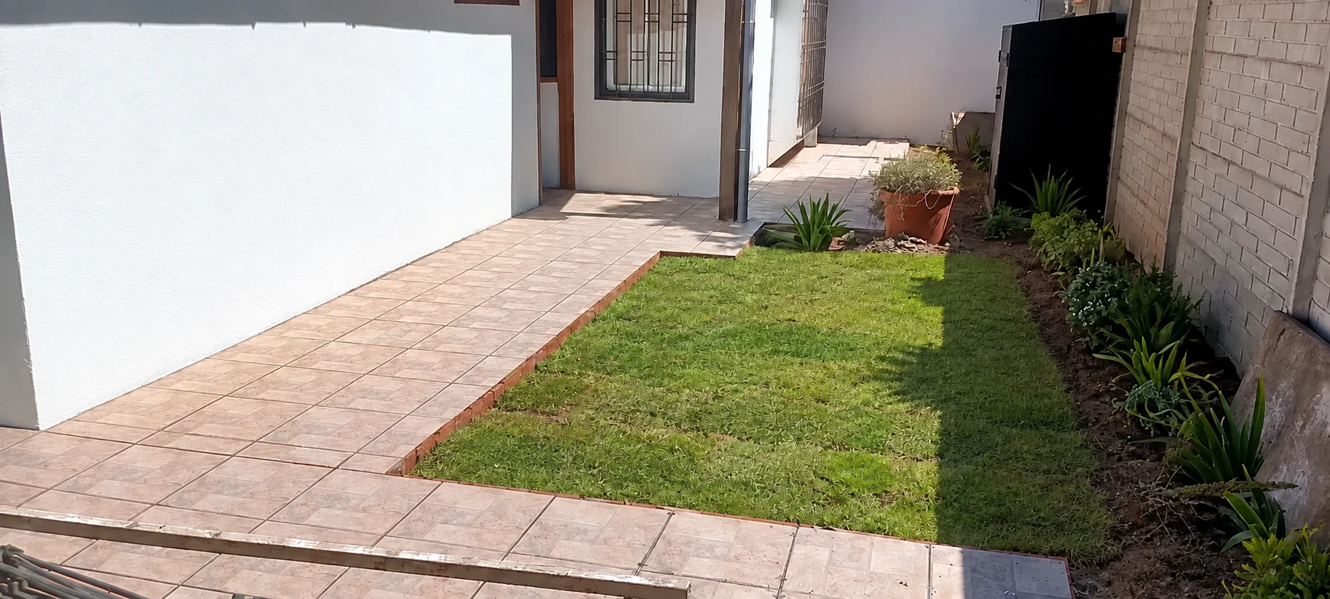 Propuesta generada con IA del patio de Lo Barnechea con pasto, plantas y la pared blanca pintada